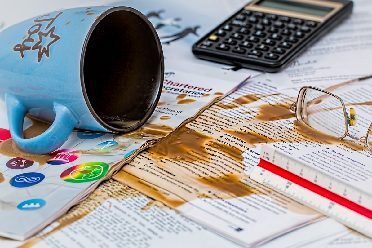 A coffee mug laying sideways, spilling coffee onto tax returns and documents.