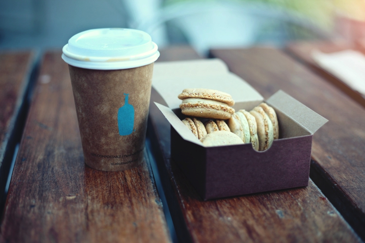 Image: A cup of coffee and a box of macaroons sit on a wooden table.