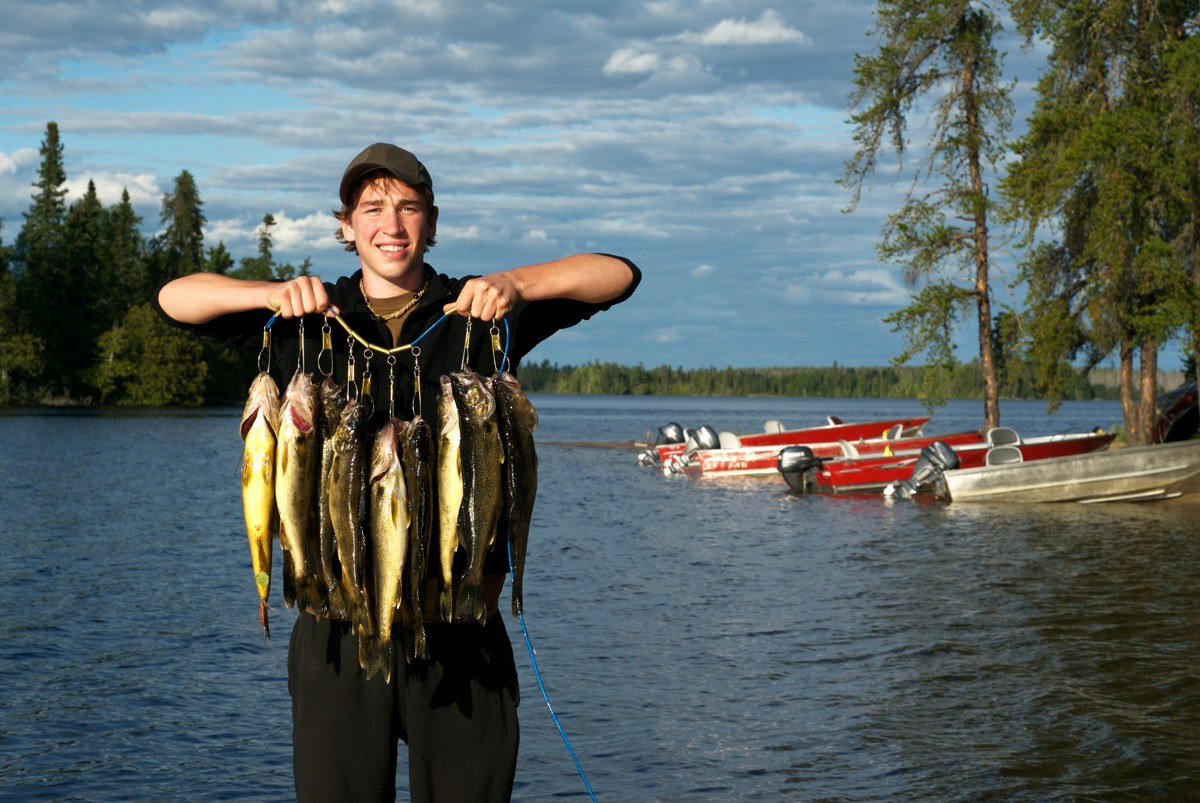 a smiling man holds up a number of fish on hooks, showing off his catch