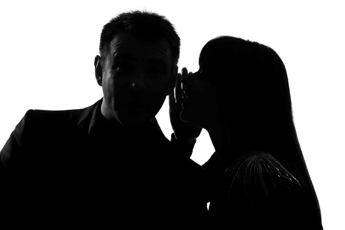 silhouette of a man and woman; the woman is whispering into the man’s ear