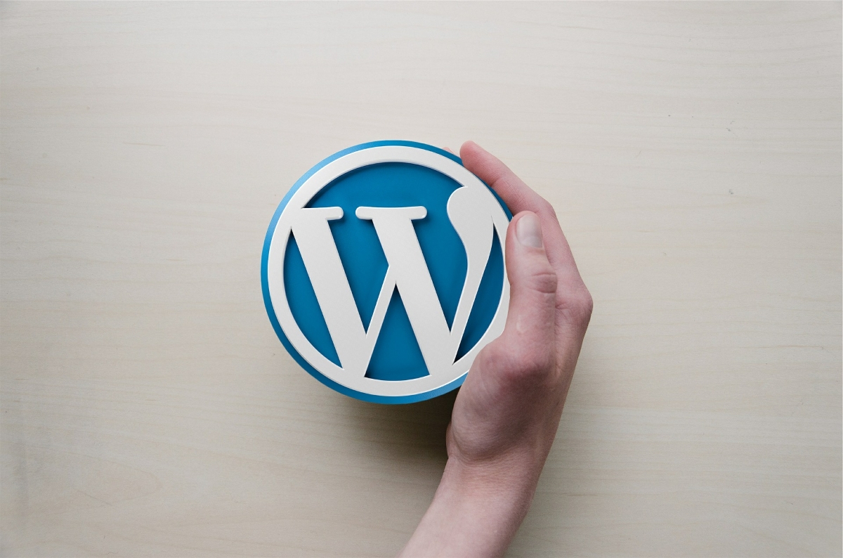 The WordPress logo on a beige background, with a hand reaching out to grasp it.